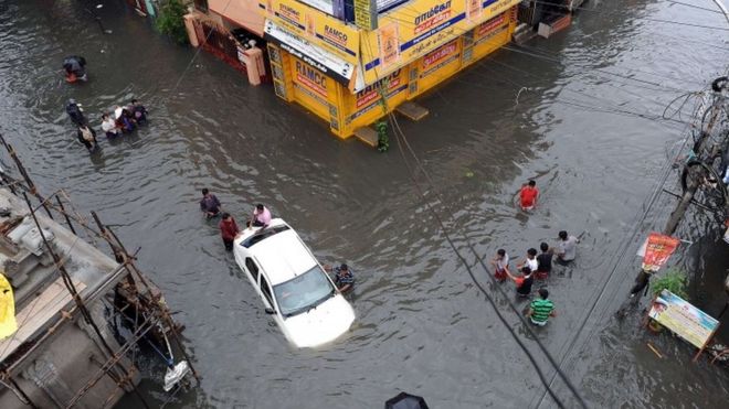 Жители Индии пытаются протолкнуть автомобиль через паводковые воды, в то время как другие проходят мимо Ченнаи 2 декабря 2015 года.