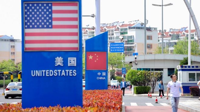 Знаки с американским флагом и китайским флагом видны в районе порта свободной торговли Циндао в Циндао в китайской восточной провинции Шаньдун 8 мая 2019 года.