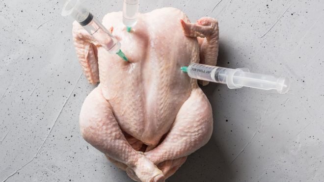 Pedaço de frango inteiro e cru com três seringas espetadas