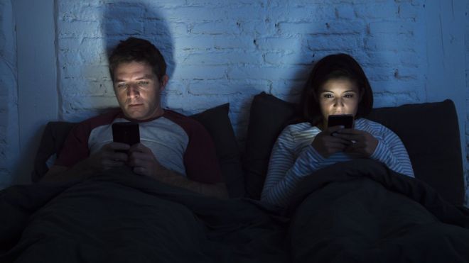 Мужчина и женщина в постели, глядя на смартфоны.