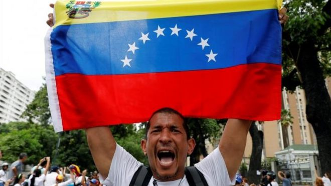 Hombre sostiene bandera de Venezuela.