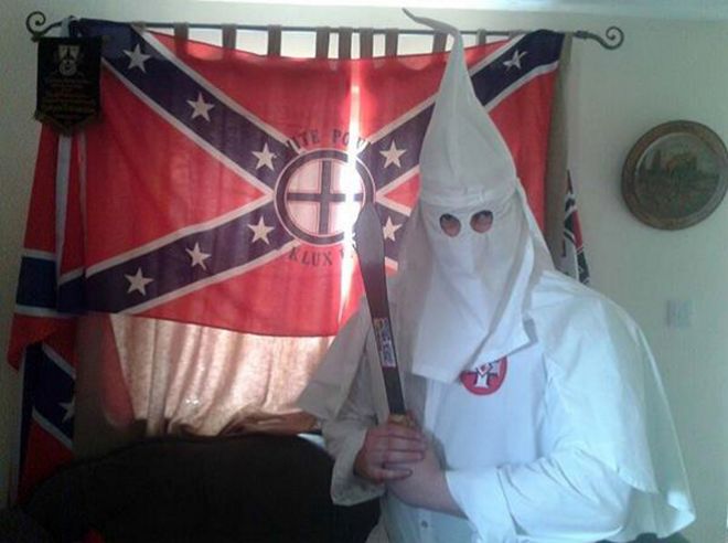 Человек в белом наряде ККК держит мачете перед флагом Конфедерации