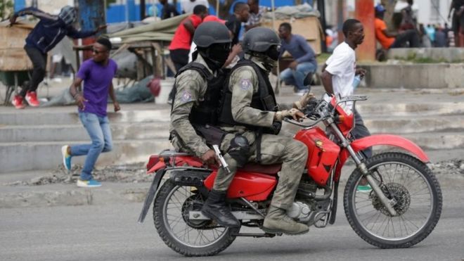 Протестующие и люди в масках в форме Гаитянской национальной полиции убегают во время перестрелки на Марсовом поле, Порт-о-Пренс, Гаити, 23 февраля 2020 года.