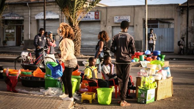 Люди и кто-то с велосипедом идут мимо уличного киоска, торгующего посудой в Асмэре, Эритрея