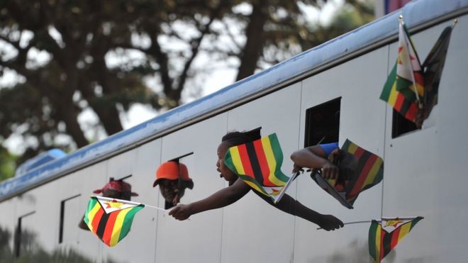 Сторонники нового президента Зимбабве машут флагами Зимбабве из автобуса, когда они прибывают в правящую штаб-квартиру Зимбабве Zanu-PF в Хараре 22 ноября 2017 года.