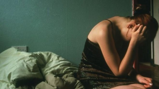Imagem mostra mulher sentada em cama, com a cabeça baixa