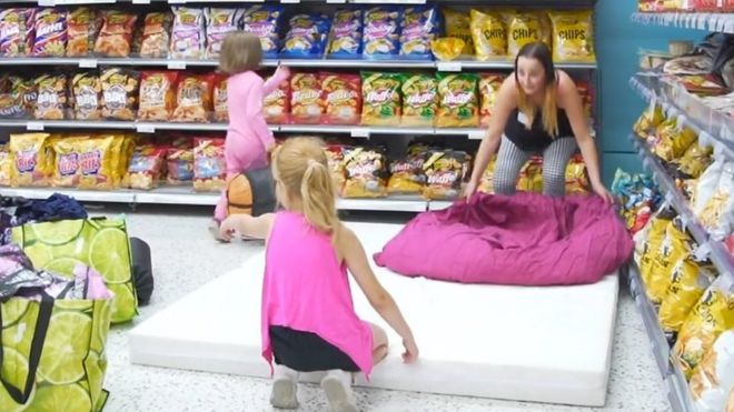 A woman and two children place a mattress near the crisps aisle
