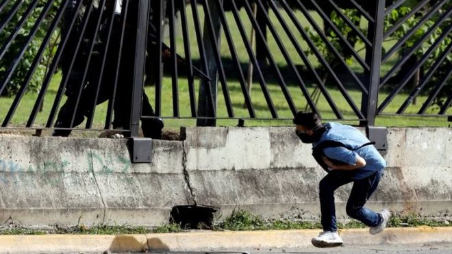 Сотрудник сил безопасности ОМОНа направляет пистолет через забор базы ВВС в Дэвиде Хосе Валленилья, который был смертельно ранен во время столкновений с митингом против правительства президента Венесуэлы Николаса Мауро в Каракасе, Венесуэла, 22 июня 2017 года.