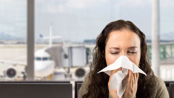 Una mujer tose en un aeropuerto.