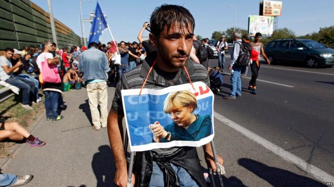 Мигрант на костылях с фотографией Ангелы Меркель на шее на автостраде в Будапеште (4 сентября 2015 года)