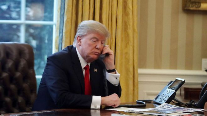 Президент Дональд Трамп виден через окно, разговаривая по телефону с королем Саудовской Аравии