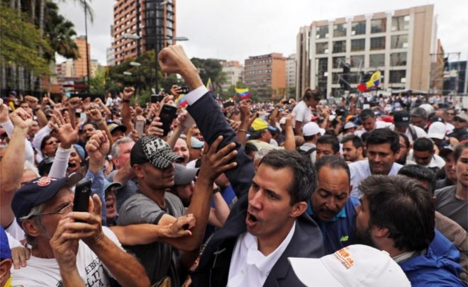 Хуан Гуайдо, президент венесуэльского парламента, приветствует толпу в Каракасе после объявления о том, что 23 января 2019 года он принимает исполнительные полномочия