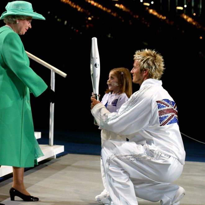 Дэвид Бекхэм и Кирсти Ховард вручают королевскую юбилейную дубинку королеве Елизавете II после того, как она завершает последний этап по стадиону города Манчестер на церемонии открытия Игр Содружества.