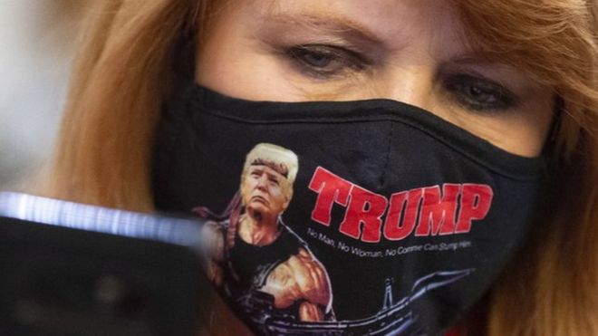 امرأة ترتدي كمامة تحمل صورة ترامب