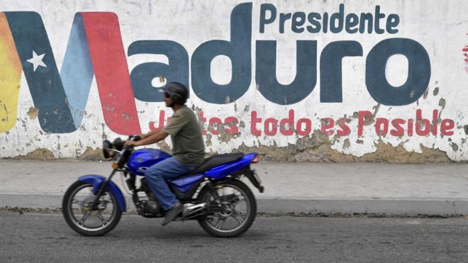 A motorcyclist rides in front of a mural with the surname of Venezuelan President Nicolas Maduro in Caracas, Venezuela