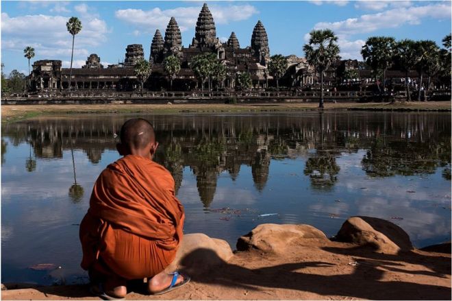 Молодой монах сидит перед нехваткой перед храмом Ангкор-Ват 1 января 2016 года, около Сием Рип, Камбоджа.