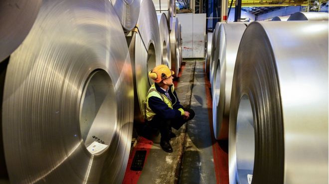 worker inspects rolls of steel