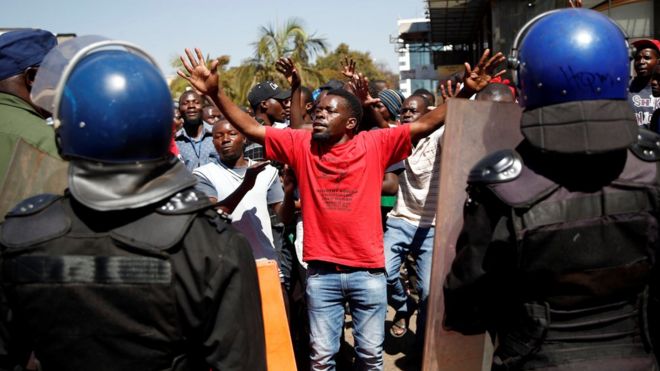 Сторонник оппозиционной партии "Движение за демократические перемены" (НДЦ) Нельсона Чамиса жестом обращается к ОМОНу, когда они маршируют по улицам Хараре, 1 августа 2018 года