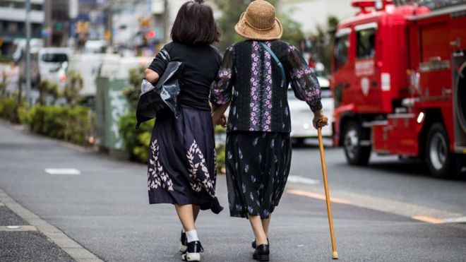 Пожилую женщину сопровождают по оживленной дороге в Токио 3 октября 2019 года.