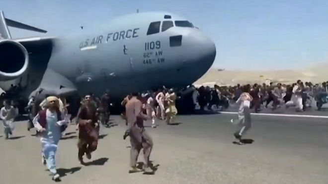 Multidão corre em volta de avião em pista de aeroporto