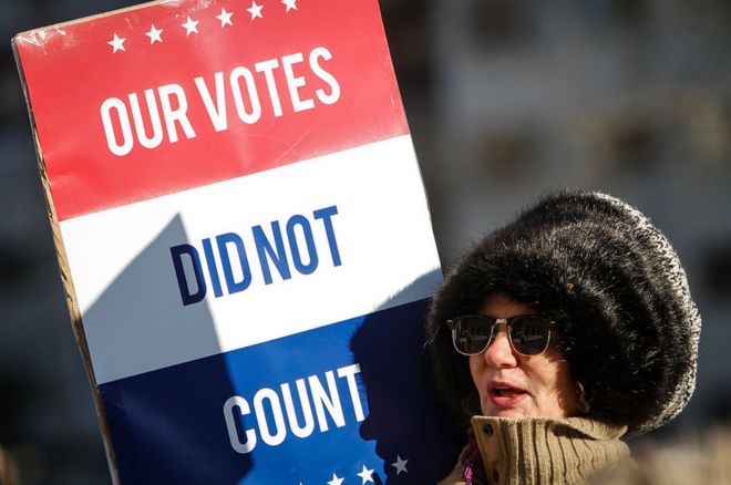 Протестующий за пределами столицы штата Мичиган осуждает избирателей, голосующих внутри в понедельник.
