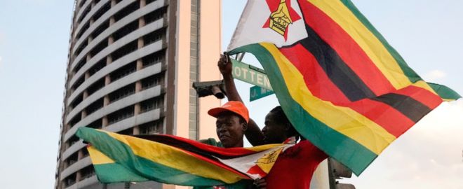 Люди с зимбабвийскими флагами празднуют на улице после отставки Роберта Мугабе на посту президента 21 ноября 2017 года в Хараре, Зимбабве