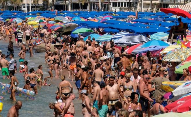 Люди освежаются на пляже во время жары в юго-восточном прибрежном городе Бенидорм