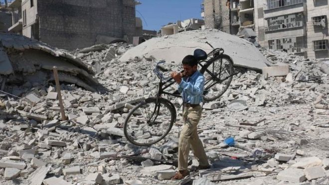Hombre lleva una bicicleta en sus hombros tras un bombardeo en Alepo.