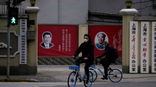 Люди в масках проходят мимо портретов президента Китая Си Цзиньпина и покойного председателя Китая Мао Цзэдуна