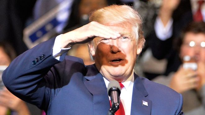 Дональд Трамп поднимает руку, чтобы защитить глаза от яркого луча света