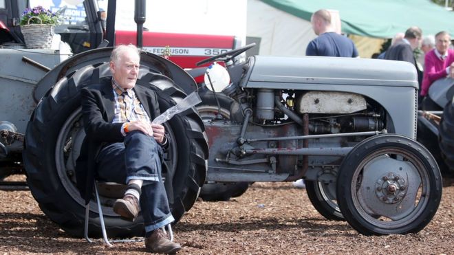 Мужчина сидит рядом со старинным трактором на выставке Balmoral