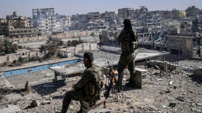 Milicianos de las Fuerzas Democráticas Sirias (SDF, por sus siglas en inglés) hacen guardia desde una azotea en un edificio en Raqa.