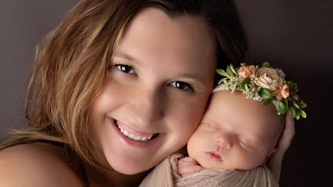 Kayla Edwards sorri segurando sua filha, Indy Pearl, que dorme