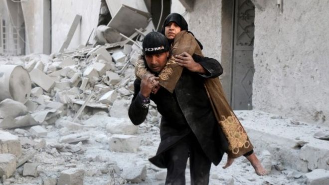 Спасатель выносит женщину из здания, подвергшегося авиаудару