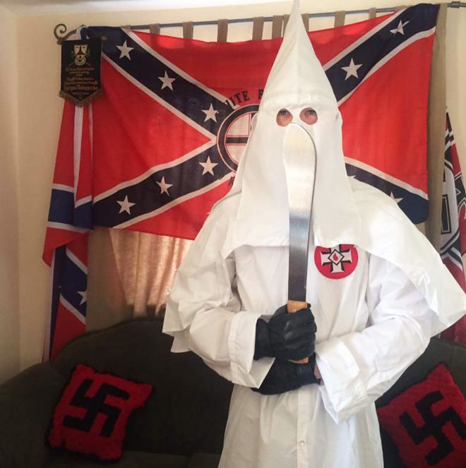 Thomas segura um machete vestido com o traje característico da Ku Klux Klan