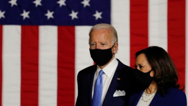 Biden e Harris de máscara em frente a bandeira americana