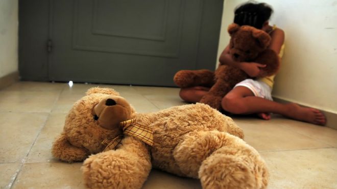 Foto ilustrativa sobre abuso infantil - menina sentada em casa com ursinho de pelúcia