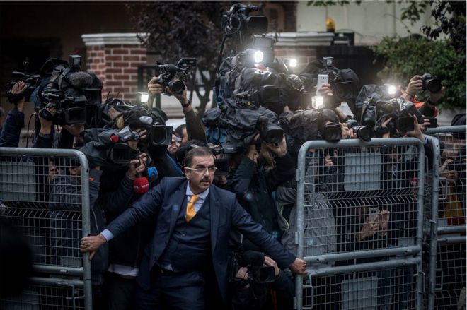 Толпа кинооператоров пытается пройти через ворота, когда мужчина их сдерживает