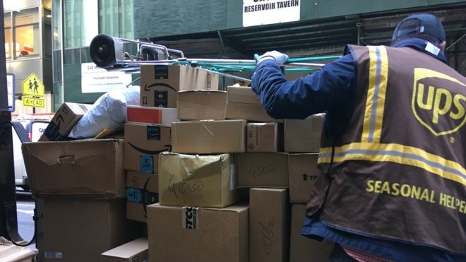 Сезонная помощь в UPS загружает тележку с ящиками в Нью-Йорке