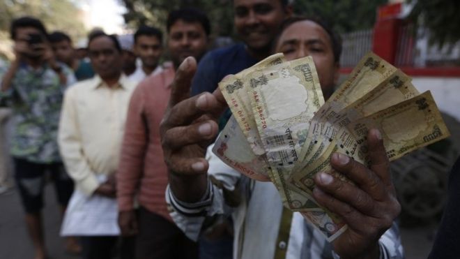 Индийский мужчина показывает банкноты в индийской валюте на сумму 1000 и 500 рупий, когда он стоит в очереди, чтобы обменять или депонировать прекращенные валютные банкноты возле почтового отделения в Ахмадабаде, Индия, четверг, 10 ноября 2016 г.