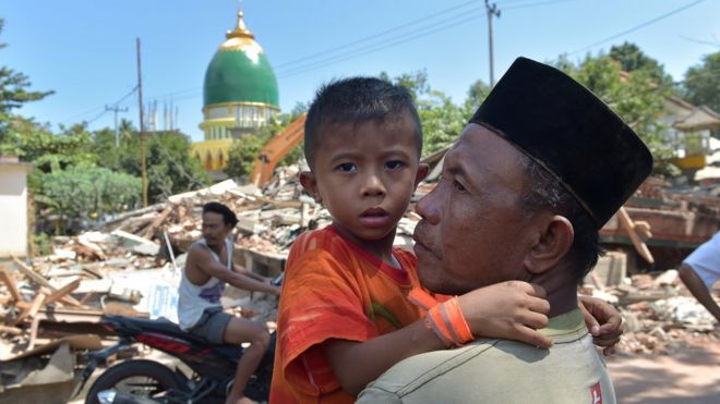 Indonežanin drži mladog dečaka ispred ruševina, Lombok, avgust 2018.
