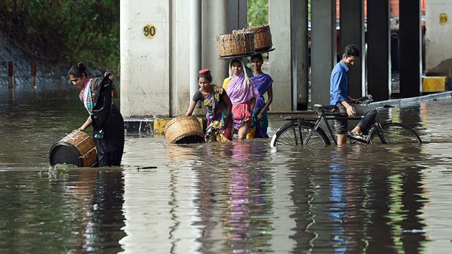 Индийские пешеходы и велосипедист идут по затопленной улице после сильного муссонного дождя в Мумбаи 21 июня 2016 года