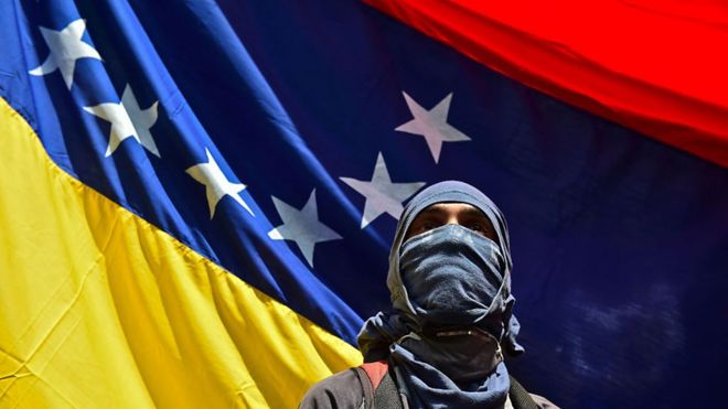 Hombre joven protestando en Venezuela con la bandera nacional de fondo