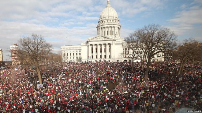 Тысячи демонстрантов протестуют возле Капитолия штата Висконсин 12 марта 2011 года в Мэдисоне, штат Висконсин. Организаторы ожидали, что 200 тысяч участников примут участие в митинге, чтобы выразить свое несогласие с законопроектом губернатора Скотта Уокера о ремонте бюджета, который по существу исключил права на заключение коллективных договоров для государственных служащих.