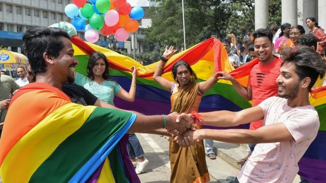 Индийские ЛГБТ-активисты и сторонники празднуют решение суда, танцуют и держат радужные флаги и воздушные шары