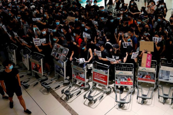 Протестующие против законопроекта об экстрадиции используют тележки, чтобы не дать пассажирам войти в ворота безопасности во время массовой демонстрации после ранения женщины в глаз в международном аэропорту Гонконга в Гонконге, Китай