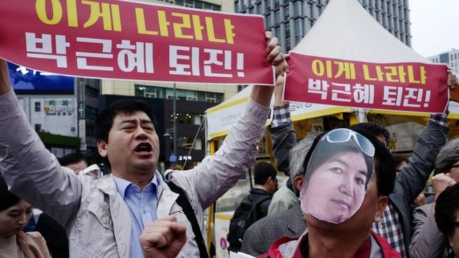 Протестующий (справа) носит вырезанную фотографию Чой Сун-Сил, а другой демонстрант держит плакат с надписью: «Отставка президента Пак Кын Хе»; в Сеуле 27 октября 2016 года