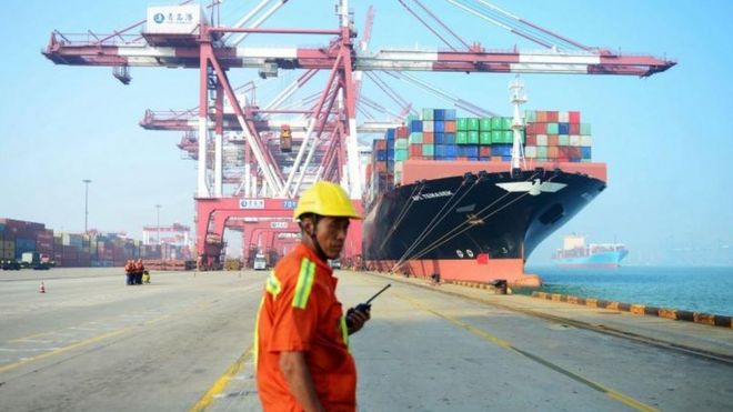 Китайский рабочий смотрит, как грузовое судно загружается в порту в Циндао