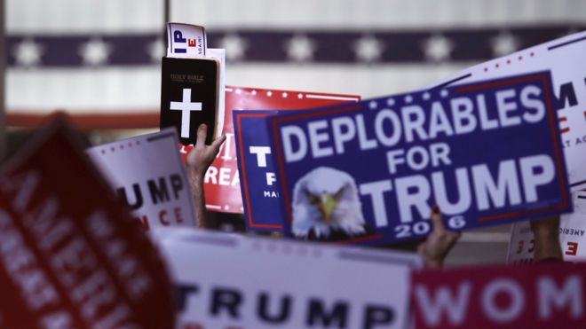 Сторонники держат в руках знаки и копию Библии во время митинга за кандидата в президенты от республиканцев Дональда Трампа, в понедельник, 7 ноября 2016 года, в Манчестере, штат Северная Каролина.