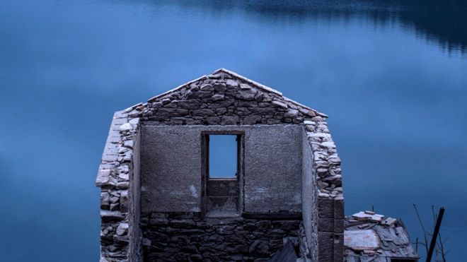 Paredes de una casa en ruinas, por una ventana se ve el lago azul
